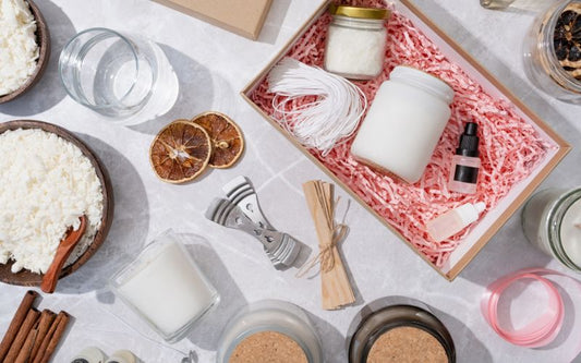Il est disposé sur une table blanche, des bougies et du matériel de fabrication de bougie ainsi qu'un coffret cadeau.