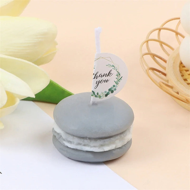 Bougie Décorative Gourmande Macaron, de couleur grise et posée sur une table. Fond beige.