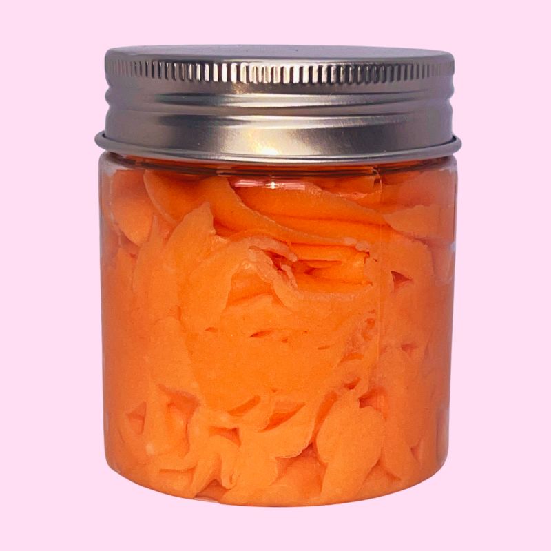Fondant Parfumé Délice de Melon Givré, de couleur orange et la senteur melon, dans un contenant fermé. Sur fond rose.