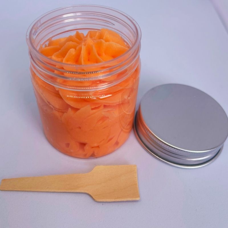 Fondant Parfumé Délice de Melon Givré, le fondant est de couleur orange, le contenant est ouvert et avec la cuillère pour le prendre. Sur fond gris.