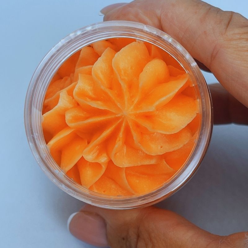 Fondant Parfumé Délice de Melon Givré, le fondant est de couleur orange et bien crémeux dans son pot. Maintenue par une personne et sur fond gris clair.