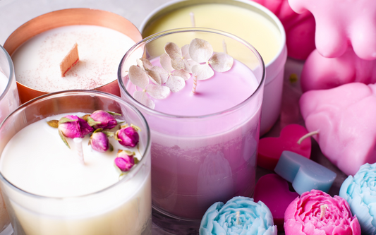 Bougie dans pot en verre de plusieurs couleurs avec des fleurs séchées à l’intérieur puis à côté des pots en verres d'autres bougies bleues et roses en vrac