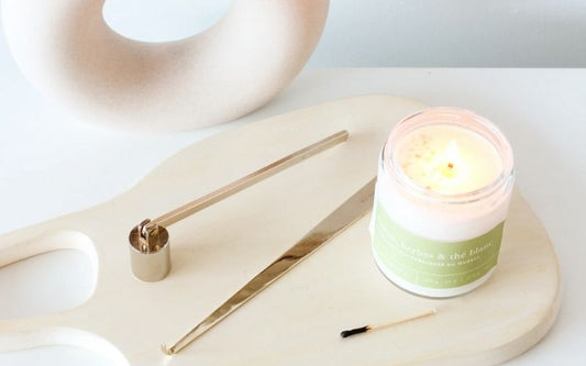 Accessoires pour bougies avec coupe-mèche et éteignoir posés près d’une bougie parfumée, ambiance minimaliste et élégante.