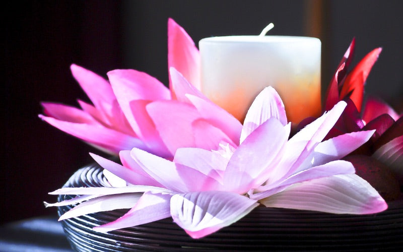 La bougie est à côté une fleur de Lys rose et légèrement violette, posée sur un support noir et dans une ambiance zen.