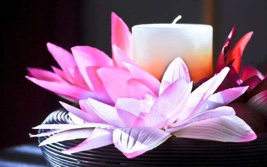 La bougie est à côté une fleur de Lys rose et légèrement violette, posée sur un support noir et dans une ambiance zen.