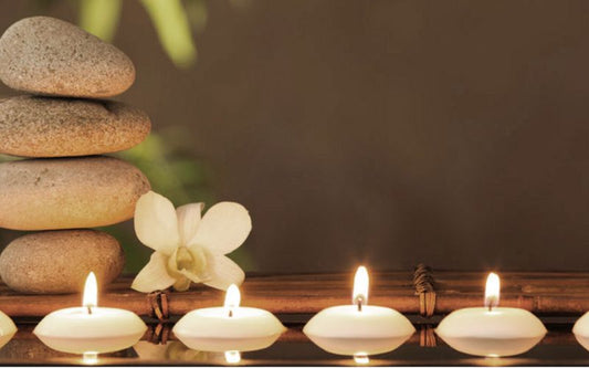 Bougies flottante allumées alignées devant des galets empilés et une fleur blanche, créant une ambiance zen et apaisante.