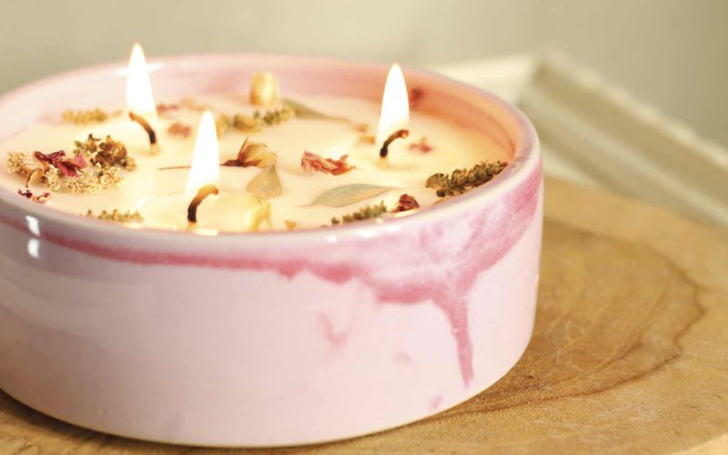 Bougie décorative allumée avec fleurs séchées dans un contenant rose pour une ambiance cosy à la maison.