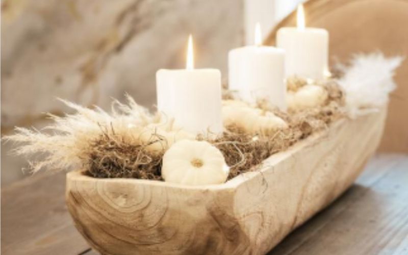 Bougies blanches décoratives allumées dans un centre de table en bois naturel, décoration intérieure chaleureuse avec fleurs séchées et ambiance cocooning.