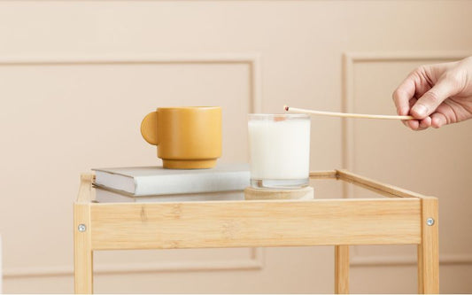 Main allumant une bougie blanche sur table en bois minimaliste, ambiance douce et chaleureuse, décoration intérieure épurée et cocooning.