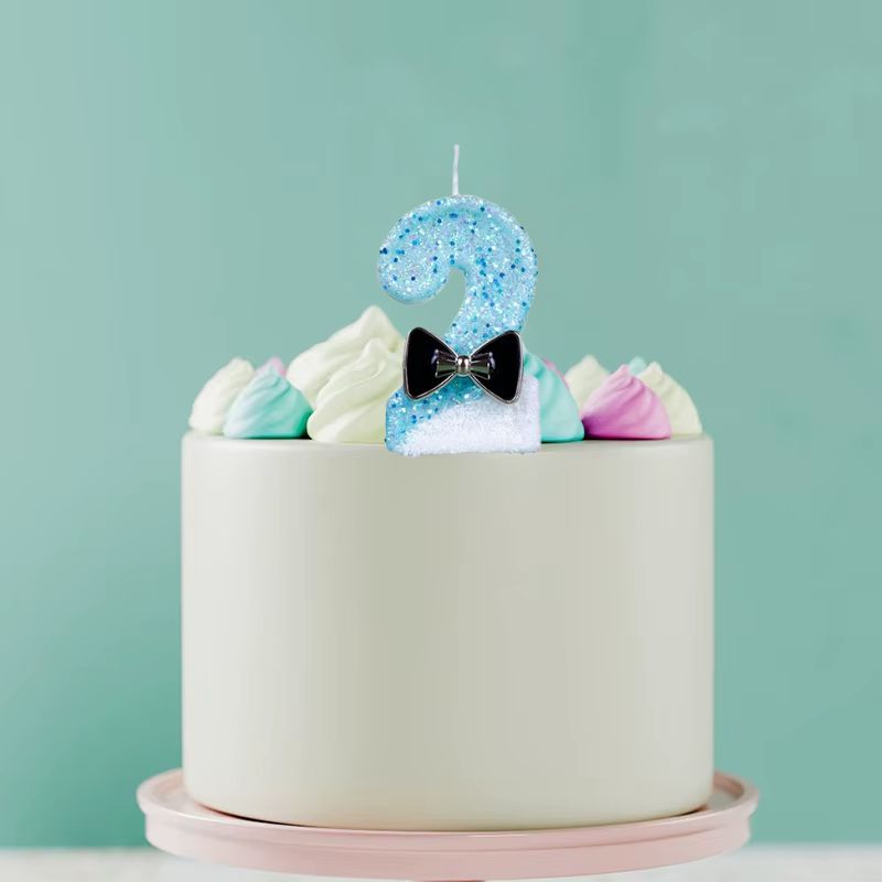 Bougie Anniversaire Charme Scintillant, disposée sur un gâteau d'anniversaire, le chiffre de la bougie est le 2. Sur fond vert.