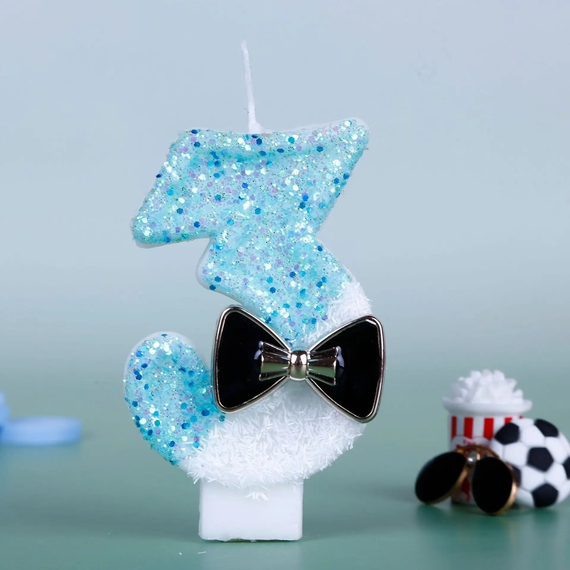 Bougie Anniversaire Charme Scintillant, le chiffre de la bougie est le 3, de couleur bleue et blanche, sur fond bleu pâle.