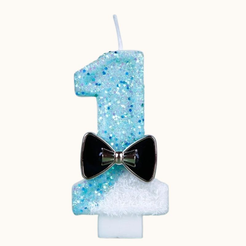 Bougie Anniversaire Charme Scintillant, le chiffre représenté est le 1, de couleur bleue et blanche avec un nœud noir. Sur fond beige clair.