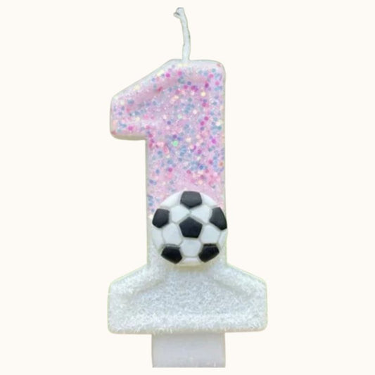 Bougie Anniversaire Coup d’Envoi Enchanté, le chiffre de la bougie est le 1, de couleur rose pailleté et blanc avec un ballon de foot dessus et sur fond beige clair.