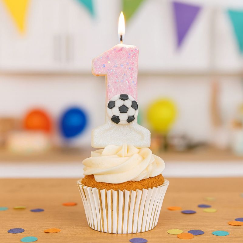 Bougie Anniversaire Coup d’Envoi Enchanté, le chiffre de la bougie est le 1, de couleur rose et blanche, posé sur un cupcake et dans une ambiance festive.