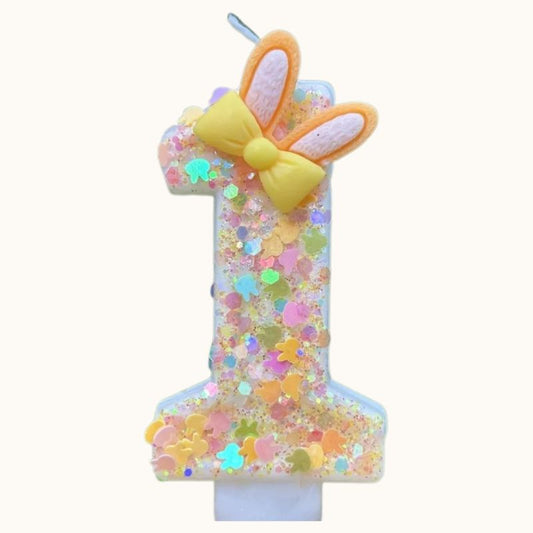 Bougie Anniversaire Douce Fantaisie, avec des paillettes multicolores, le chiffre de la bougie est le 1 et sur fond beige.