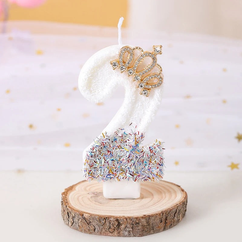 Bougie Anniversaire Édition Prestige, le chiffre de la bougie est le 2, de couleur blanche avec une couronne dorée et posée sur un rondin de bois.