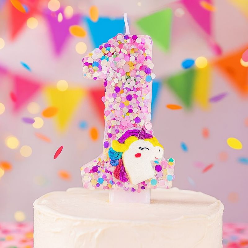 Bougie Anniversaire Licorne Explosion de Paillettes, la bougie est sur un gâteau d'anniversaire, son chiffre est le 1 et dans une ambiance festive.