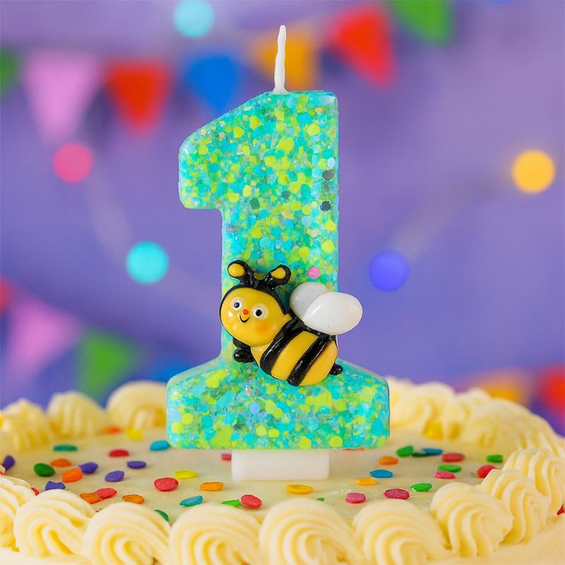 Bougie Anniversaire Magie du Jardin, le chiffre représenté est le 1, de couleur verte avec une abeille sur celle-ci et posée sur un gâteau d'anniversaire. Ambiance festive.