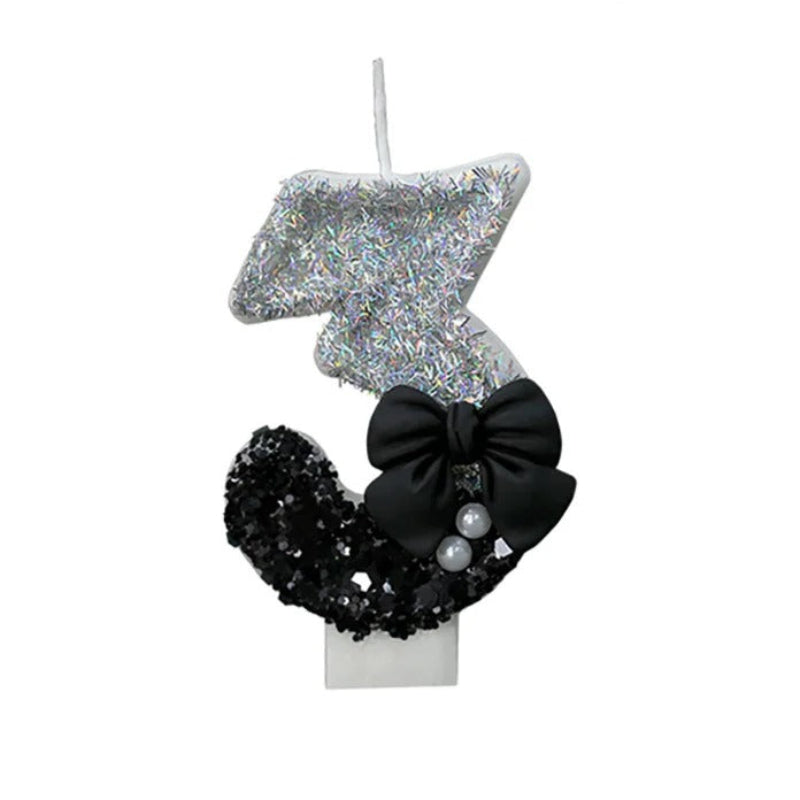 Bougie Anniversaire Nœud Chic, le chiffre représenté est le 3 , de couleur noire et grise avec un noeud et des paillettes. Sur fond blanc.