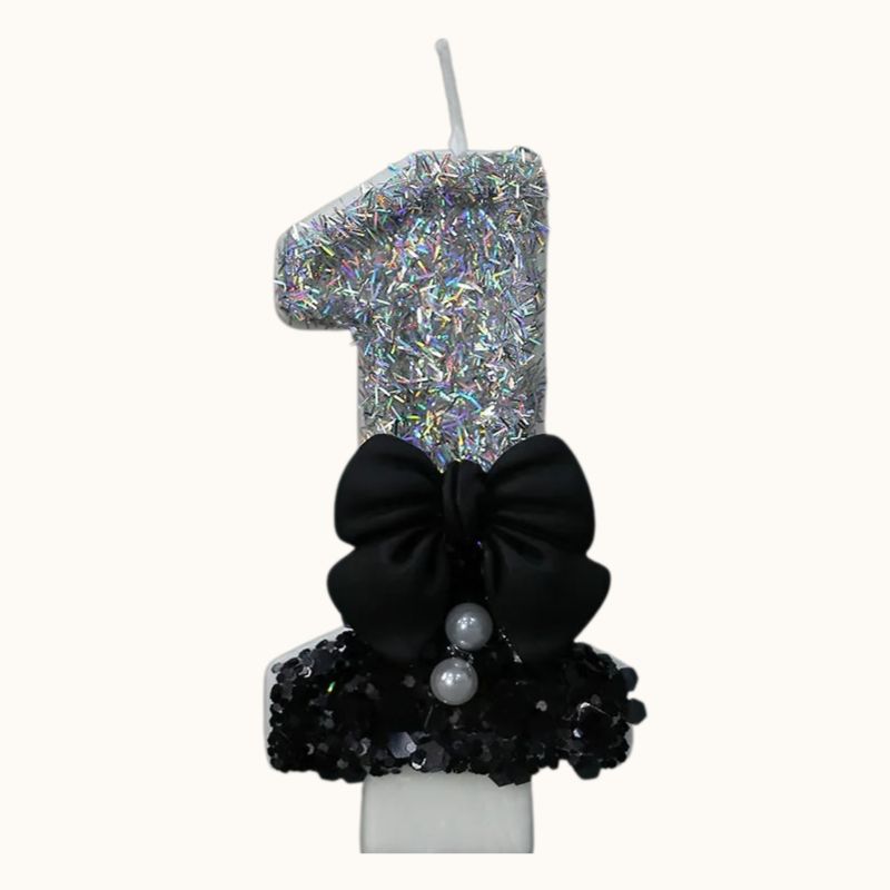 Bougie Anniversaire Nœud Chic, le chiffre est le 1, de couleur noire et argentée, avec un noeud et sur fond beige clair.