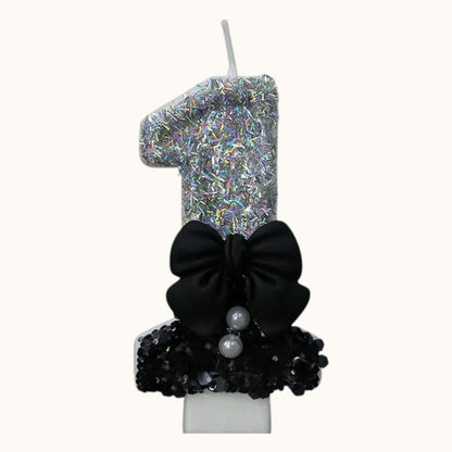 Bougie Anniversaire Nœud Chic, le chiffre est le 1, de couleur noire et argentée, avec un noeud et sur fond beige clair.