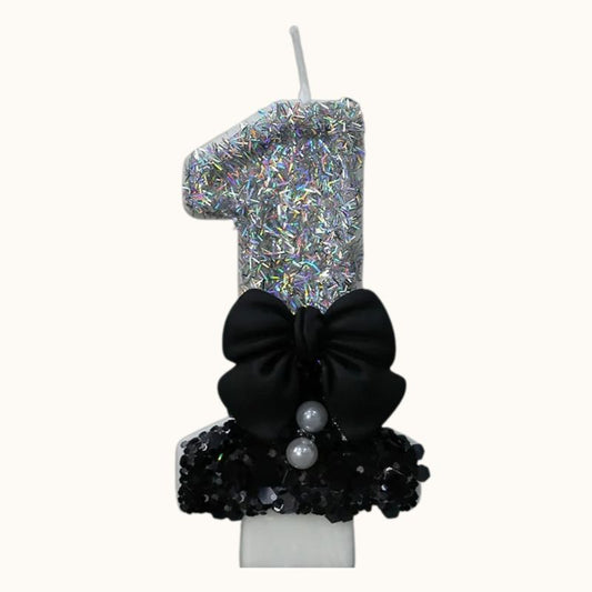 Bougie Anniversaire Nœud Chic, le chiffre est le 1, de couleur noire et argentée, avec un noeud et sur fond beige clair.