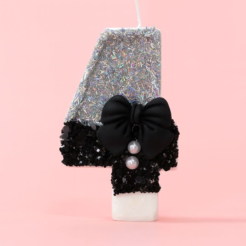 Bougie Anniversaire Nœud Chic, le chiffre représenté est le 4, de couleur noire et grise, avec un noeud et des paillettes. Sur fond rose pastel.