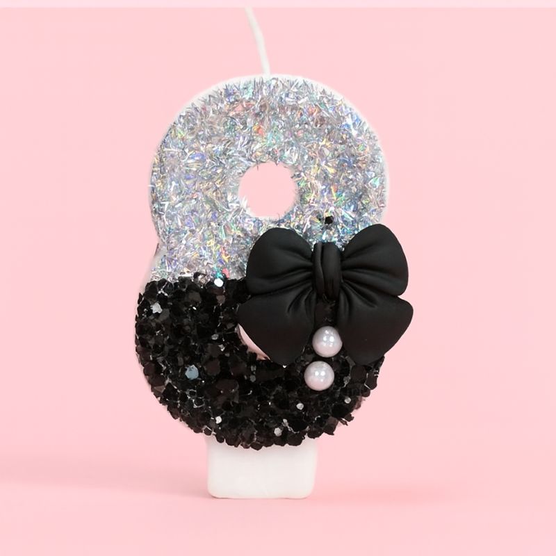 Bougie Anniversaire Nœud Chic, le chiffre représenté est le 8, de couleur noire et grise, avec un noeud et des paillettes. Sur fond rose pastel.