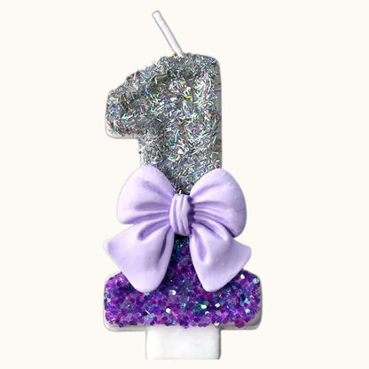 Bougie Anniversaire Noeud Romantique, le chiffre est le 1, de couleur violette et argenté, avec un noeud et des paillettes. Sur fond beige clair.