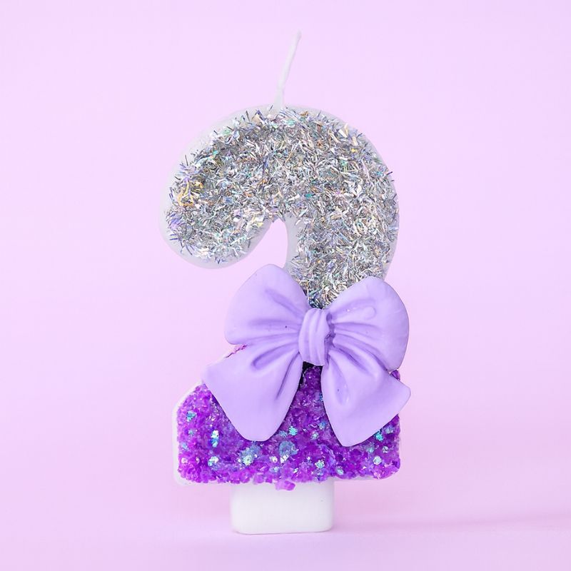 Bougie Anniversaire Noeud Romantique, de couleur violette et argentée, avec un noeud, le chiffre représenté est le 2. Sur fond violet pastel.