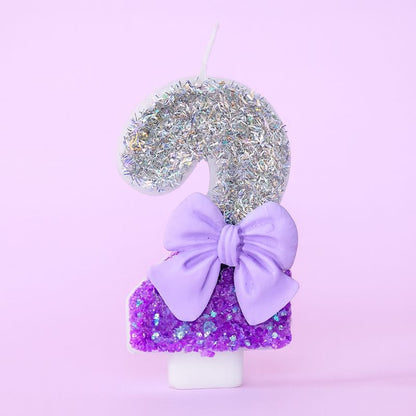 Bougie Anniversaire Noeud Romantique, de couleur violette et argentée, avec un noeud, le chiffre représenté est le 2. Sur fond violet pastel.