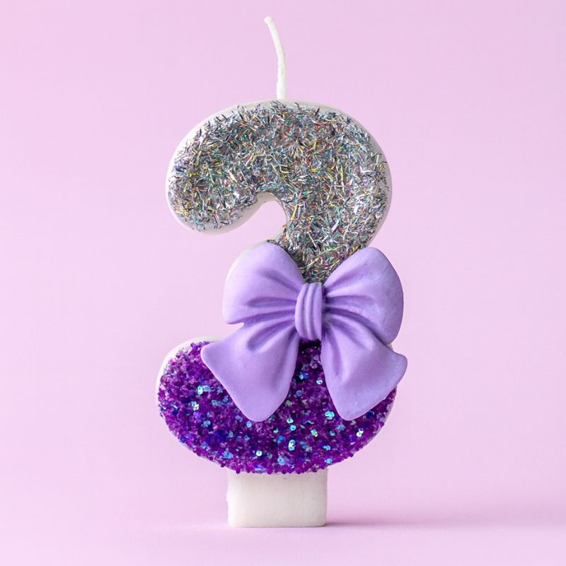Bougie Anniversaire Noeud Romantique, de couleur violette et argentée, avec un noeud, le chiffre représenté est le 3. Sur fond violet pastel.