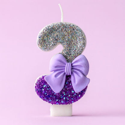 Bougie Anniversaire Noeud Romantique, de couleur violette et argentée, avec un noeud, le chiffre représenté est le 3. Sur fond violet pastel.
