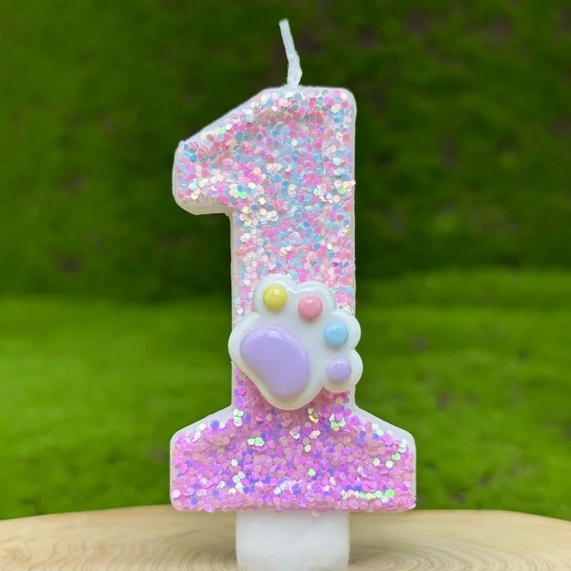 Bougie Anniversaire Patte Féline Scintillante, de couleur rose avec une patte d’animal dessus, le chiffre représenté est le 1 et sur fond vert.