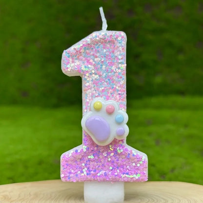 Bougie Anniversaire Patte Féline Scintillante, de couleur rose avec une patte d’animal dessus, le chiffre représenté est le 1 et sur fond vert.