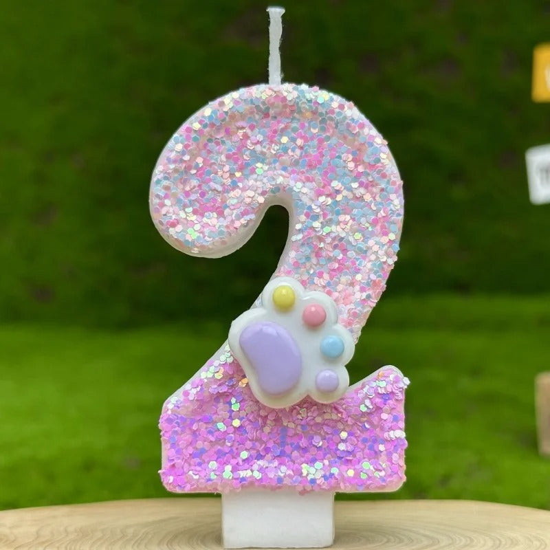 Bougie Anniversaire Patte Féline Scintillante, de couleur rose avec une patte d’animal dessus, le chiffre représenté est le 2 et sur fond vert.