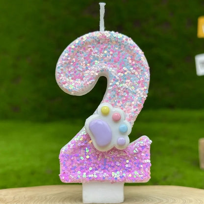 Bougie Anniversaire Patte Féline Scintillante, de couleur rose avec une patte d’animal dessus, le chiffre représenté est le 2 et sur fond vert.
