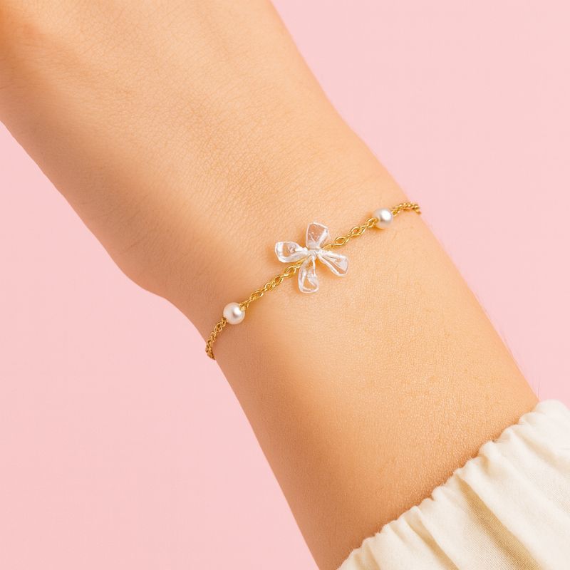 Bougie Bijou Artisanale Gourmande, on peut voir le bracelet, sur un poignet, qui se cache dans la bougie chantilly. Fond rose pâle.