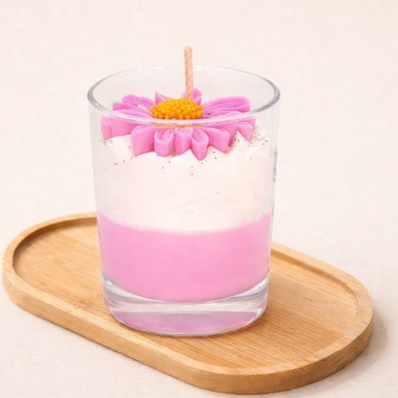 Bougie Bijou Douce Attention, la bougie est de couleur rose et blanche posée sur un plateau en bois et sur fond beige clair.