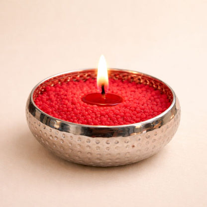 Bougie cire perle rouge bol argenté allumée décoration intérieure et sur fond beige clair.