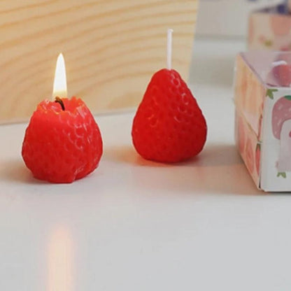 Bougie Décorative Fruit Fraise, de couleur rouge, allumée et posée sur une table.