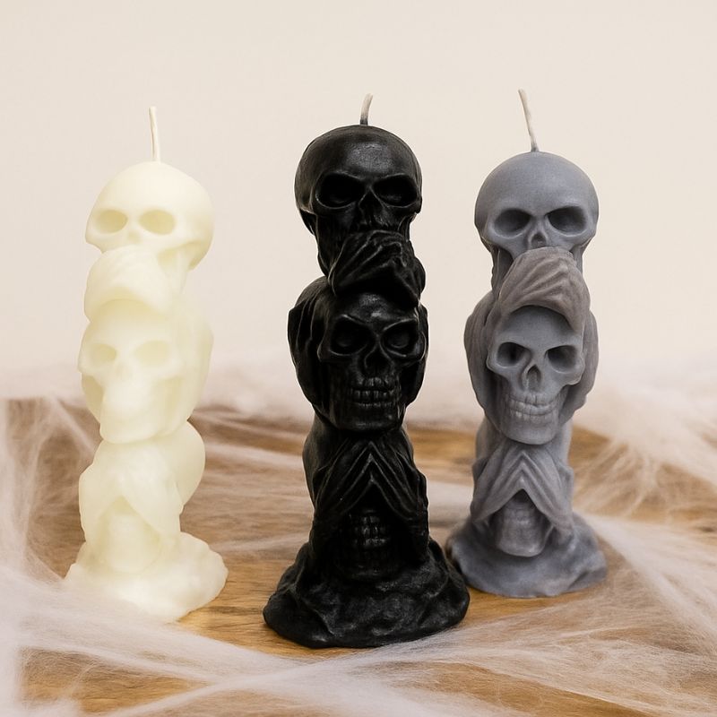 Bougie Halloween Décor Macabre, les trois couleurs sont représentées, blanc, gris et noir. Leur forme est tête de mort, posées sur une table en bois avec des toiles d'araigné autour.