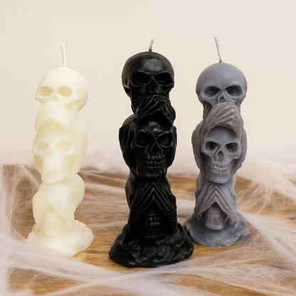 Bougie Halloween Décor Macabre, les trois couleurs sont représentées, blanc, gris et noir. Leur forme est tête de mort, posées sur une table en bois avec des toiles d'araigné autour.
