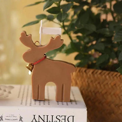 Bougie Noel Féérie du Renne Enchanté, de couleur marron et posée sur un livre. Ambiance zen.