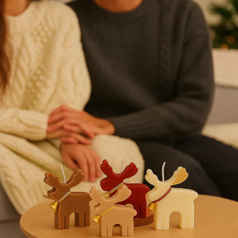 Bougie Noel Féérie du Renne Enchanté, il y a plusieurs couleurs représentées, rouge, beige, blanc et marron. On peut voir 2 adultes assis sur un canapé en arrière-plan.