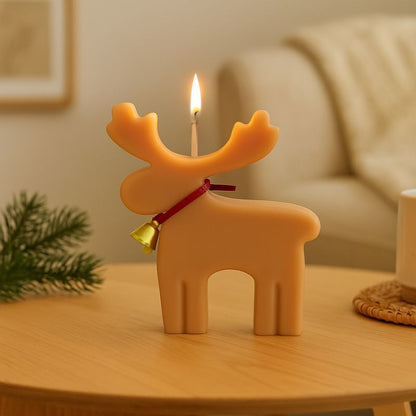 Bougie Noel Féérie du Renne Enchanté, de couleur beige clair et la bougie est allumée. Elle est posée sur une table en bois. Ambiance scandinave.