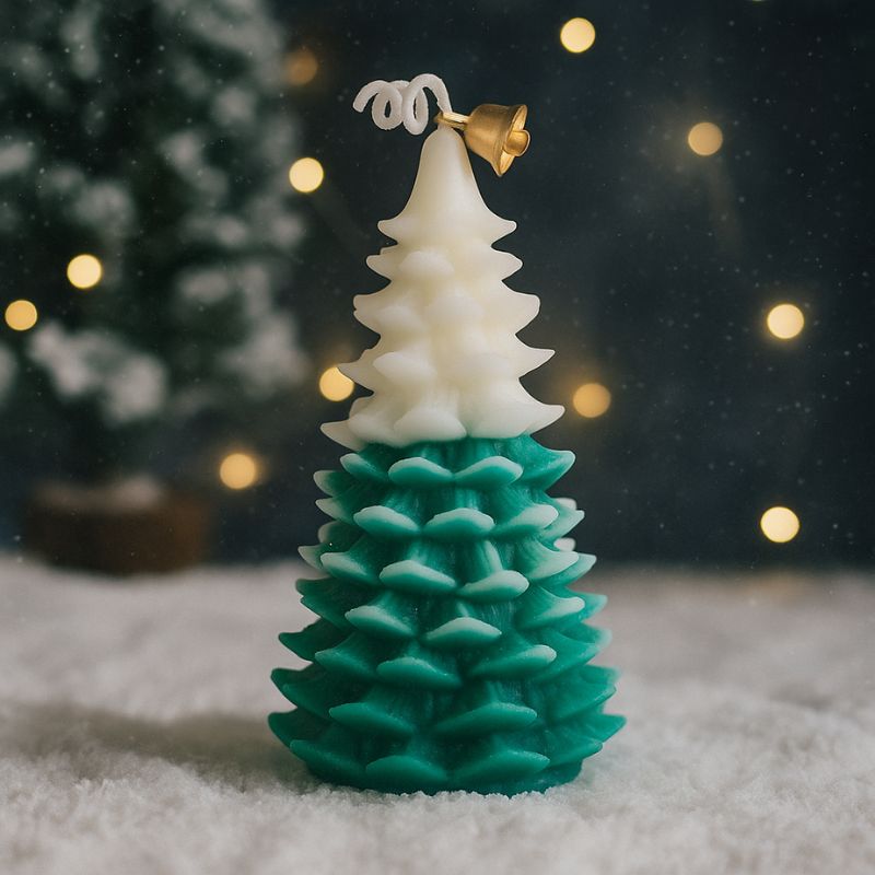 Bougie Noël Magique et Sapin Senteur d’Hiver, de couleur blanche et verte, cette bougie est posée sur de la fausse neige. Avec des lumières en arrière-plan.