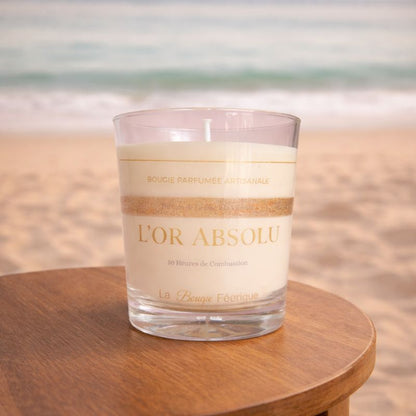 Bougie Parfumée Artisanale L’Or Absolu posée sur une table en bois face à la mer, ambiance douce et apaisante, décor naturel et lumineux évoquant un moment de détente et d’évasion.