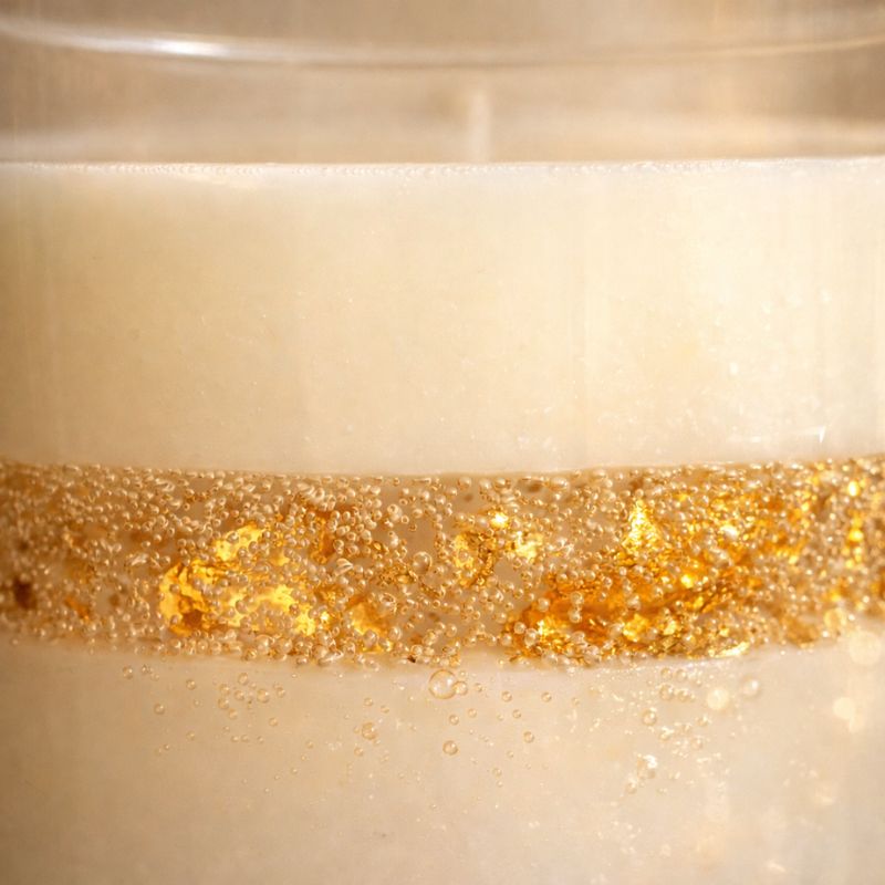 Détail Bougie Parfumée Artisanale L’Or Absolu, cire blanche avec inclusions de feuilles d’or scintillantes et bulles délicates, rendu lumineux et texture précieuse sur fond neutre élégant.