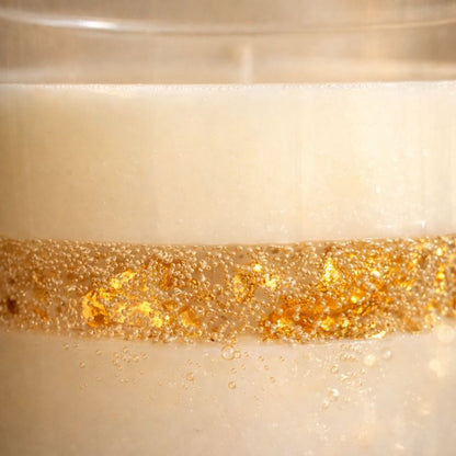 Détail Bougie Parfumée Artisanale L’Or Absolu, cire blanche avec inclusions de feuilles d’or scintillantes et bulles délicates, rendu lumineux et texture précieuse sur fond neutre élégant.
